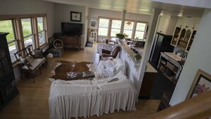 A spacious living room with a large window, a fireplace, and a kitchen area visible through an open doorway. - 3 Bedroom Farm Home. Sleeps 10 - One Mile Outside Joseph, Oregon. The Evans Farm (Joseph)