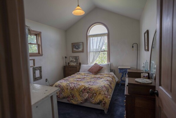 Une chambre à coucher comprenant un lit, une commode, une coiffeuse et une fenêtre donnant sur un paysage agréable.