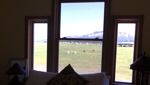 A bedroom with a large arched window overlooking a grassy field and mountains. - 3 Bedroom Farm Home. Sleeps 10 - One Mile Outside Joseph, Oregon. The Evans Farm (Joseph)