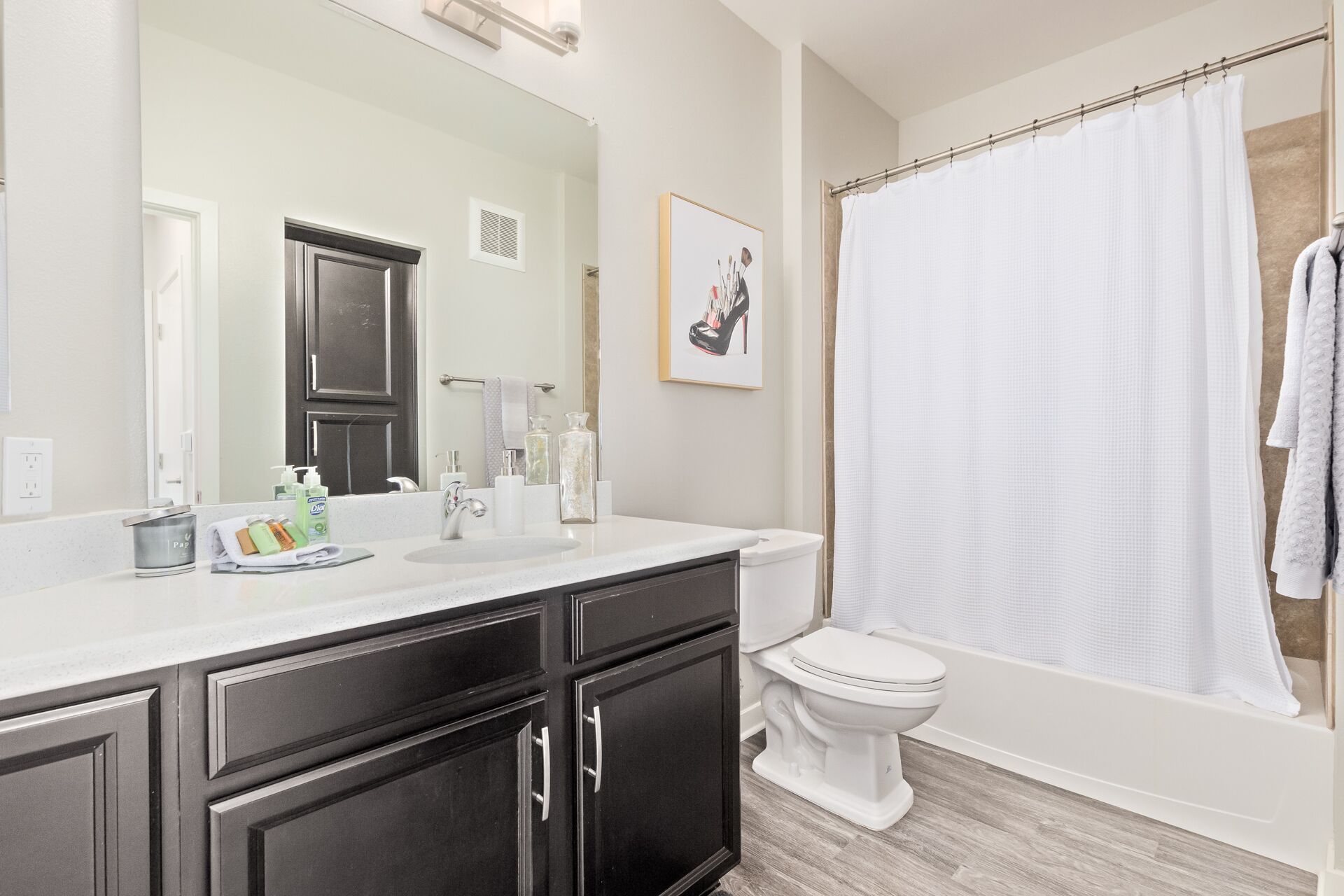 A bathroom with a white sink, dark cabinets, a toilet, and a shower curtain.