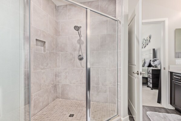A modern bathroom with a glass-enclosed shower, tiled walls, and a visible door leading to another room.
