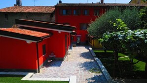 A courtyard with a stone pathway leading to a red building with a tiled roof. - CaMé (Alzano Lombardo)