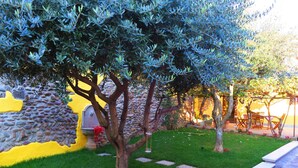 A garden with a stone wall, a yellow-painted wall, and a pathway leading to outdoor seating. - CaMé (Alzano Lombardo)