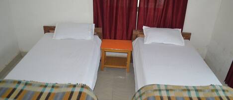 A room with two single beds, a small wooden table, and red curtains.