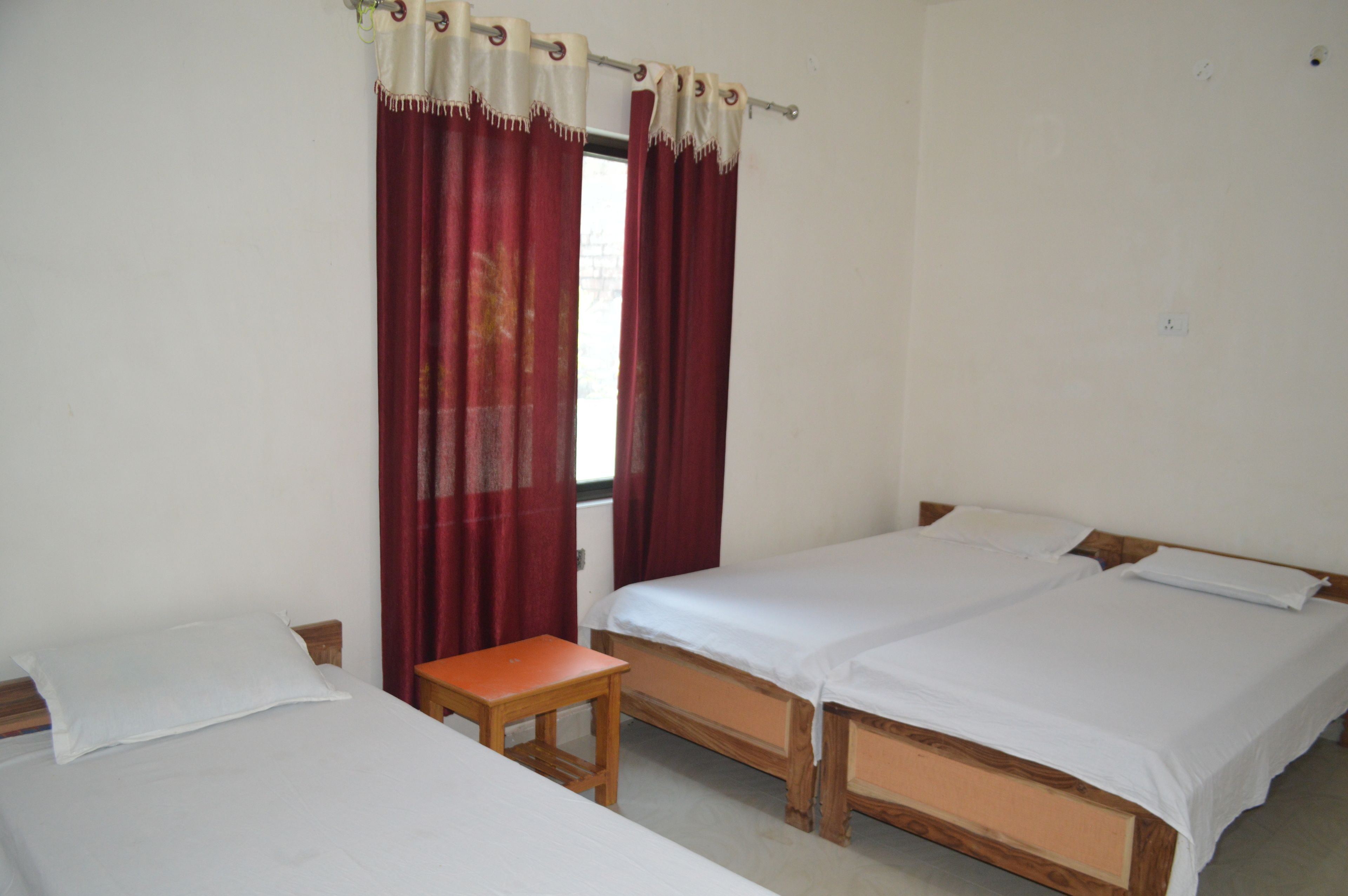 A room with two single beds, a small wooden table, and red curtains.