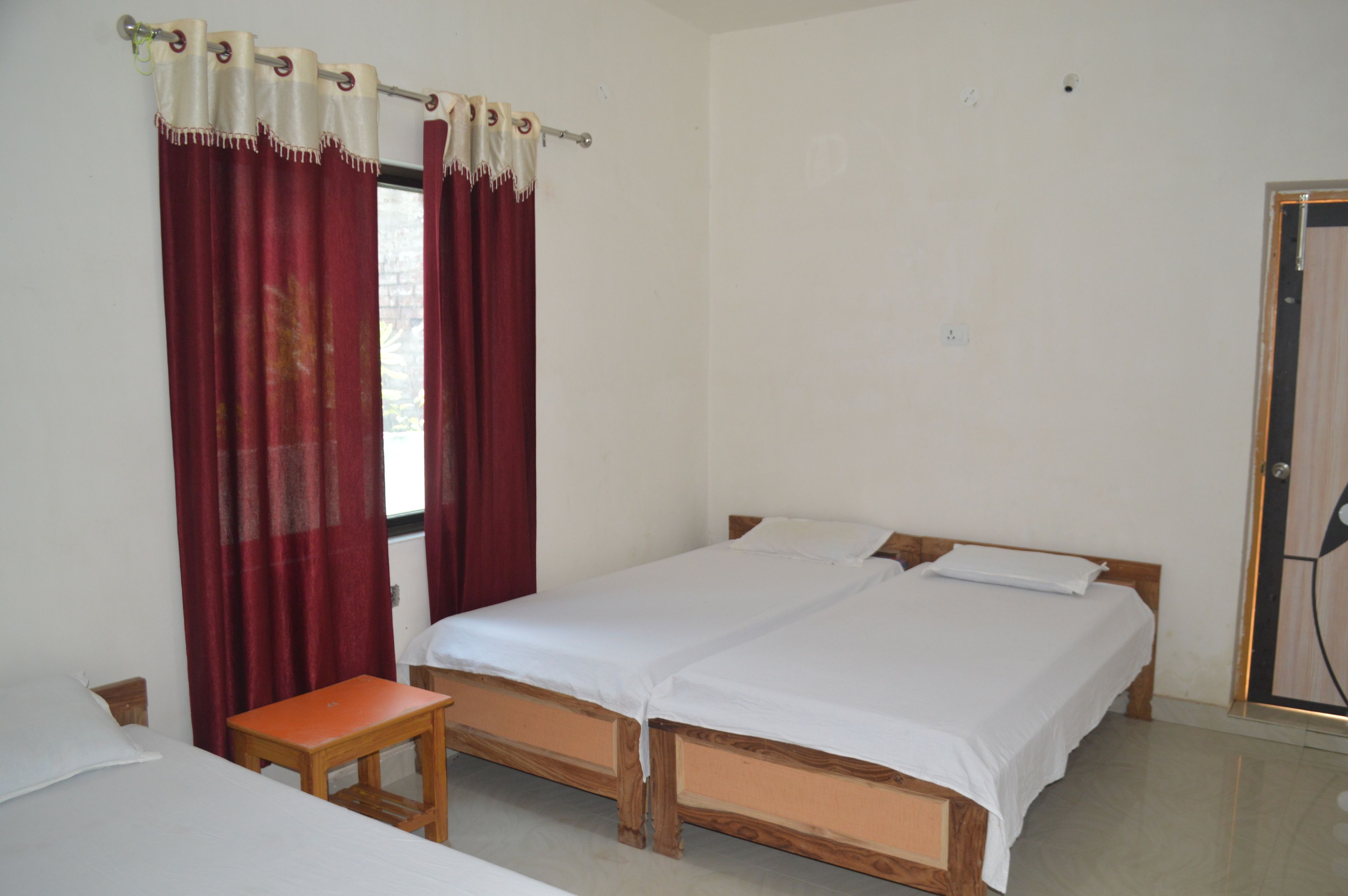 A simple, clean room with two single beds, a small table, and a window with red curtains.