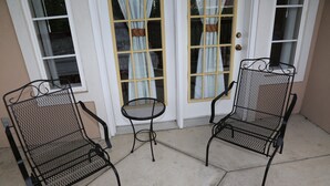 Two metal chairs and a small round table outside a building with a white door and windows. - Grand Crowne golf course view Branson Surrey w/master hot tub! (Branson)