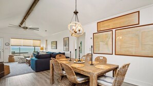 Ein geräumiger Essbereich mit Holztisch und Korbstühlen, Deckenventilator und gerahmten Kunstwerken an den Wänden.