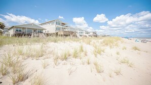 Ein Strandgrundstück mit einem großen Haus, einer Holzterrasse und einem Strand im Hintergrund.