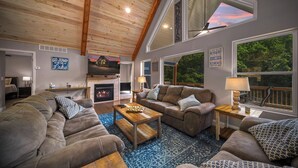 Un salon chaleureux avec une cheminée, des sièges confortables et de grandes fenêtres donnant sur le paysage extérieur.