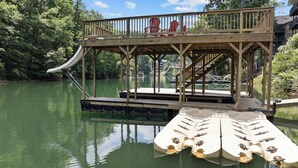 Eine Holzterrasse mit roten Stühlen und einer Rutsche über dem Wasser.