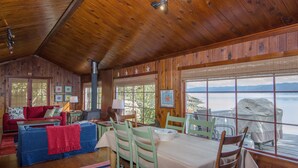 Een chalet met een houten interieur, een eethoek met tafel en stoelen, een bank en uitzicht op het meer.