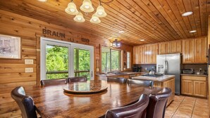 A wooden cabin interior with a large dining table, wooden cabinets, and a kitchen area. - Braun Rio - Guadalupe River, 2 King Master Suites, Loft, Riverfront Patio (New Braunfels)