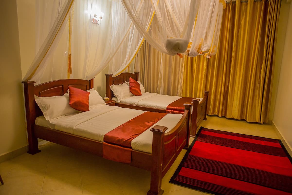 A double bed with a wooden frame and a red runner, a smaller single bed with a wooden frame, and a red and black striped rug.