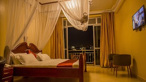 Habitación de hotel con cama, televisor montado en la pared, balcón con cortinas y una silla.