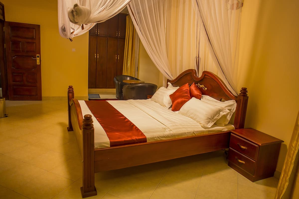 A neatly made bed with a wooden frame and a red and white bedspread, a wooden nightstand with drawers, and a chair in a room with yellow walls and a wooden door.