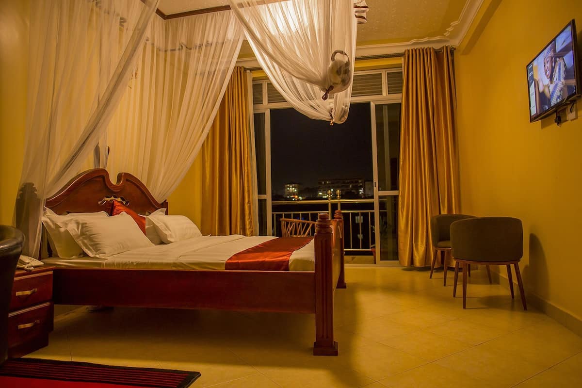 A bedroom with a bed, a TV, a chair, and a balcony with curtains.