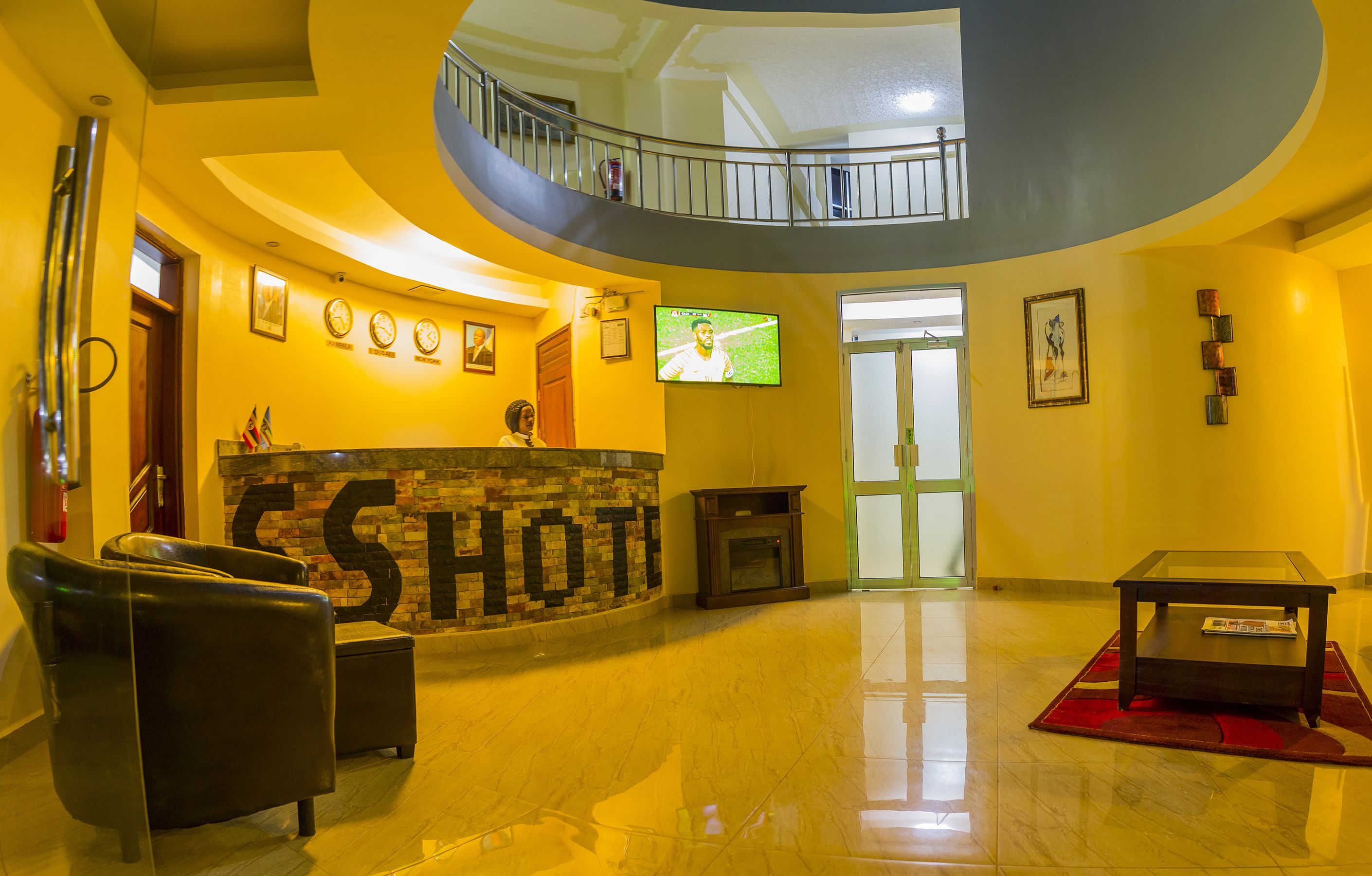 A hotel lobby with a reception desk, a television, a fireplace, and a staircase to an upper level.