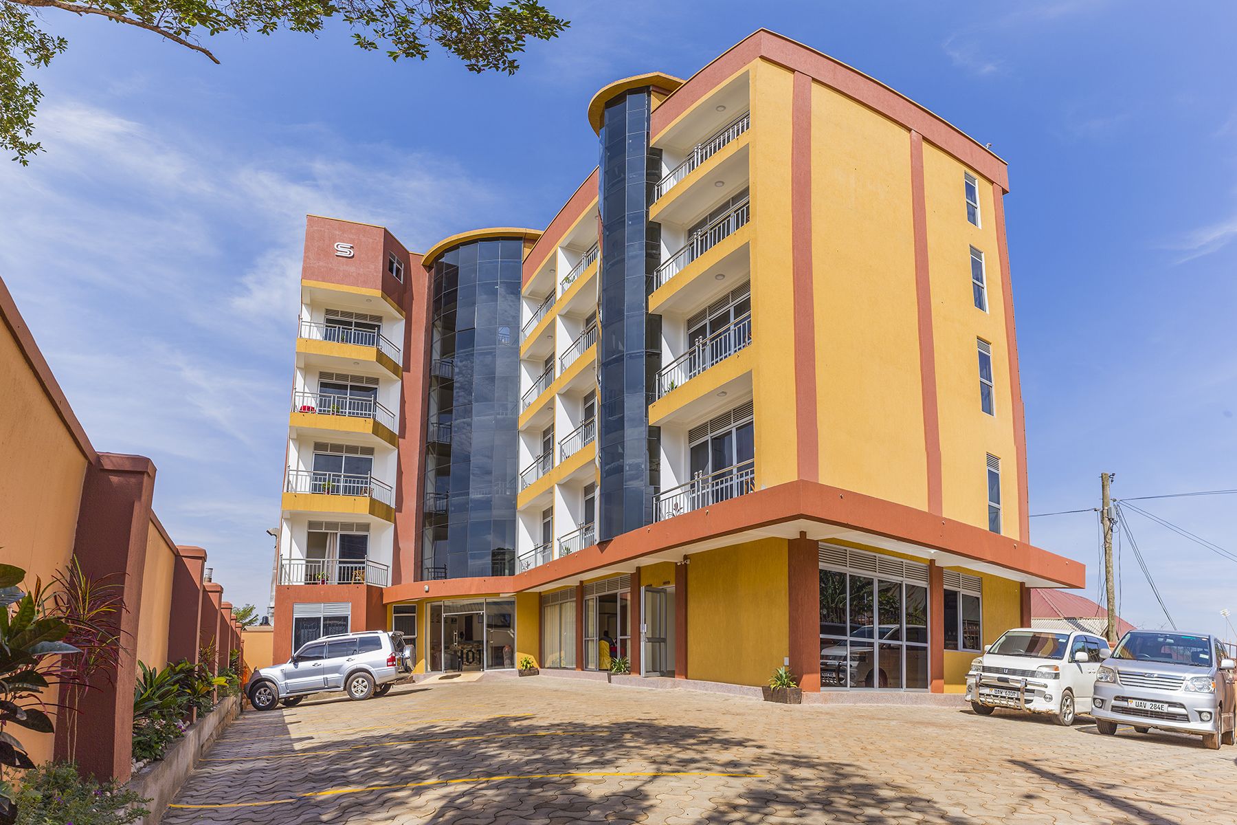 A multi-story hotel with a yellow facade, balconies on each floor, and a central glass elevator shaft.
