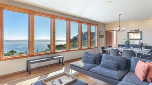 A spacious living room with a large window offering a view of the ocean and hills.