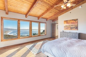A bedroom with large windows, a bed, a dresser, and a ceiling fan.