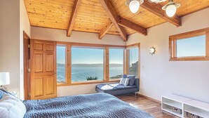 A bedroom with a large bed, a seating area with a view of the sea, and a wooden ceiling.