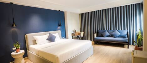 A modern hotel room with a large bed, a sofa, a desk, and a potted plant.
