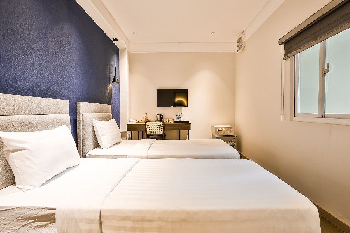 A hotel room with two beds, a desk, a chair, a TV, and a window.