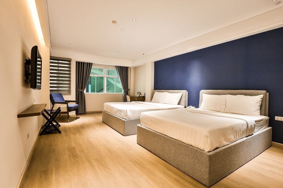 A hotel room with two beds, a desk, and a TV mounted on the wall.