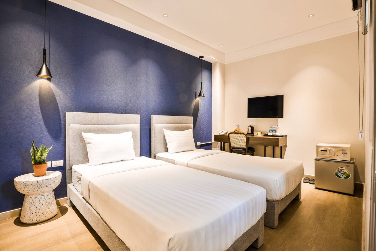 A hotel room with two beds, a desk, a TV, and a refrigerator.