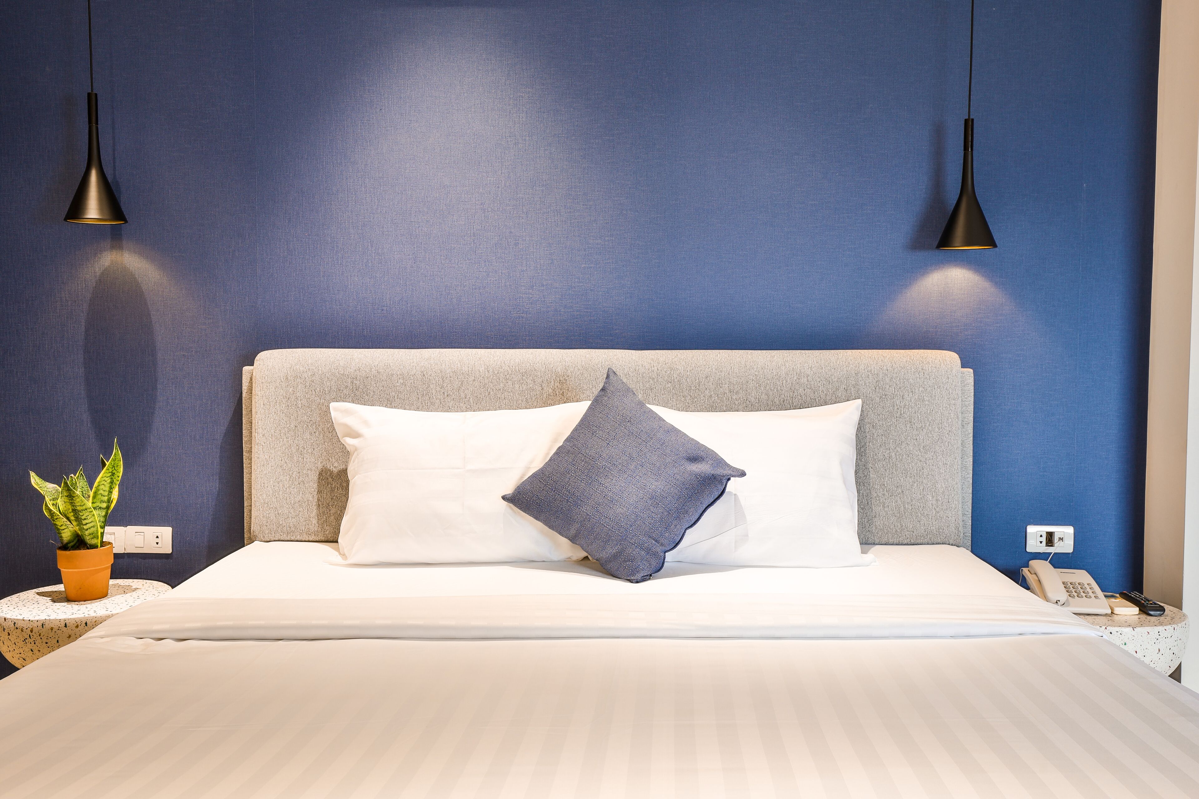 A neatly made bed with white linens, a grey headboard, and two bedside lamps.