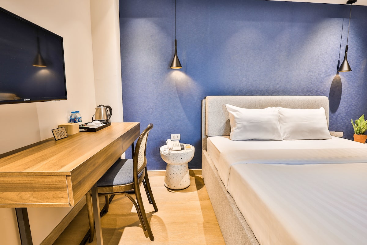 A hotel room with a bed, a desk, a chair, a toilet, and a TV mounted on the wall.