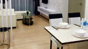 A modern living room with a white brick wall, a flat-screen TV mounted above a fireplace, a dining table with chairs, and a sofa. - Symphony Suite Malacca (Malacca City)