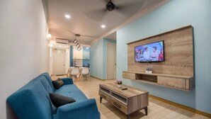 A modern living room with a blue sofa, a wooden coffee table, and a mounted TV on the wall. - Symphony Suite Malacca (Malacca City)