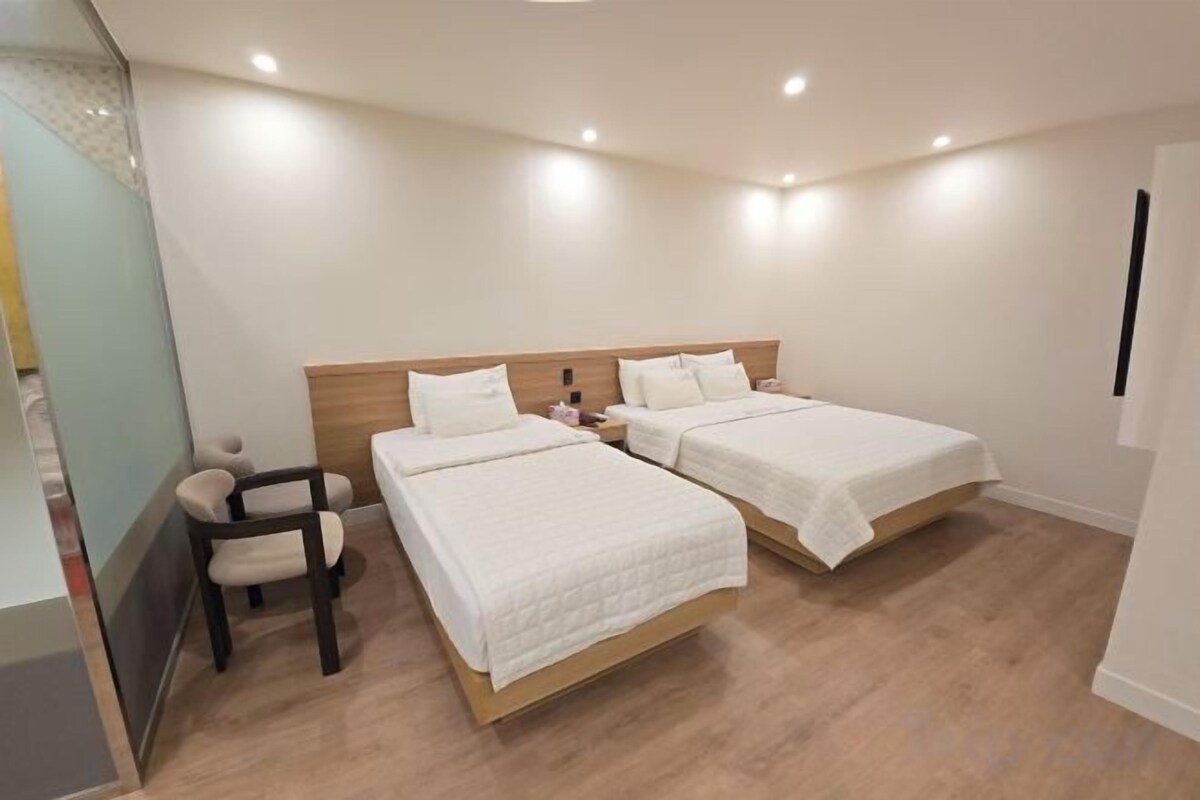 A hotel room with two beds, a desk, and a chair.