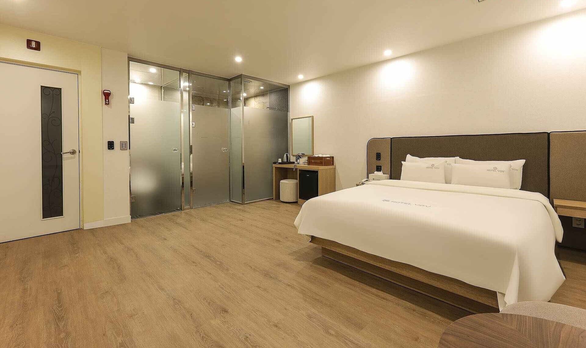 A hotel room with a bed, a desk, a mirror, and a door.