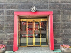 Entrada de hotel con marco rojo, puertas de vidrio y un cartel con el nombre del hotel.