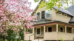 Une maison à deux étages avec un balcon, un porche à l’avant et un petit jardin devant.