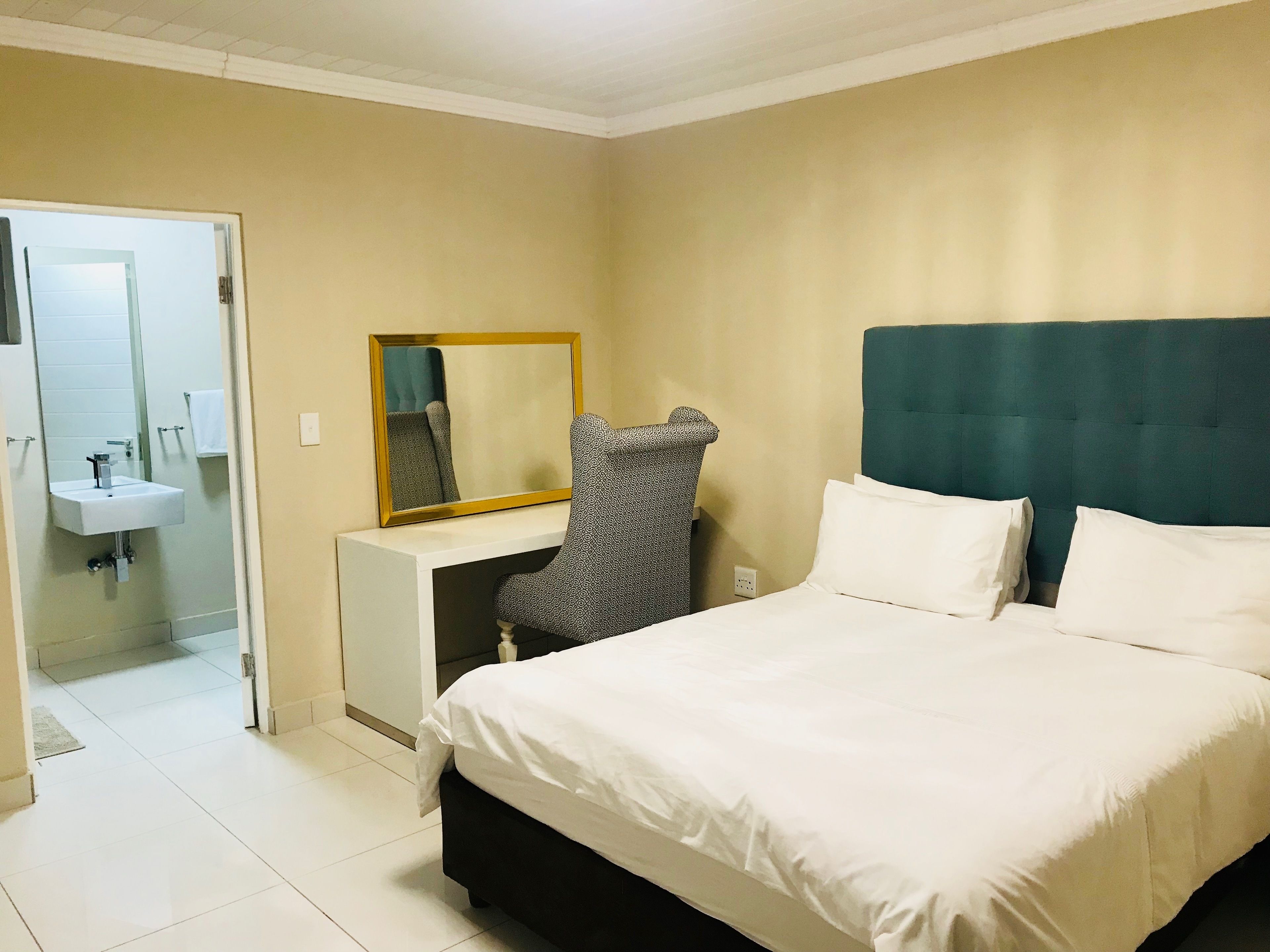 Une chambre d’hôtel comprenant un lit, un bureau avec une chaise, un miroir et une salle de bain avec un lavabo.