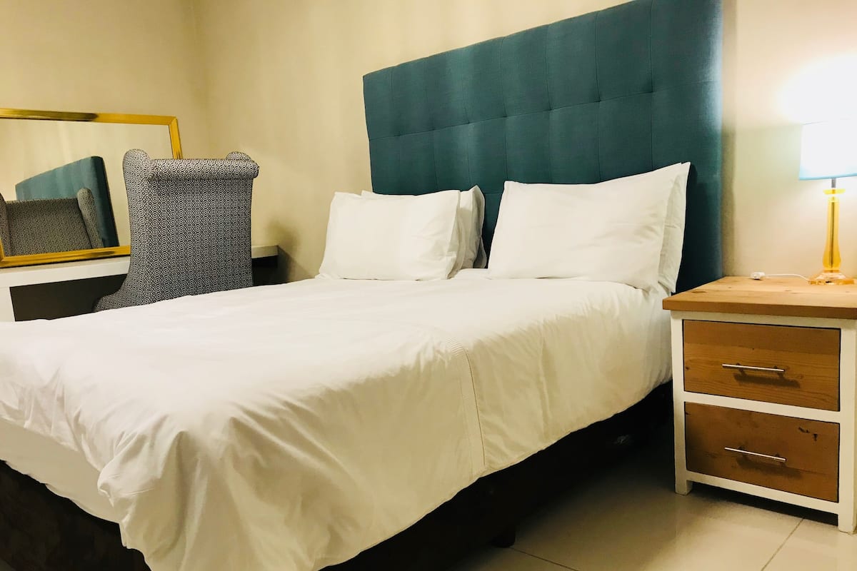 A neatly made bed with white linens, a dark headboard, and a bedside table with a lamp.