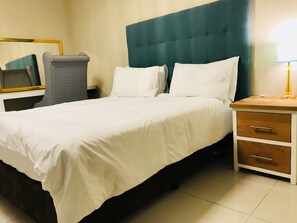 A neatly made bed with white linens, a dark headboard, and a bedside table with a lamp. - Sunset Beach Guesthouse (Cape Town)
