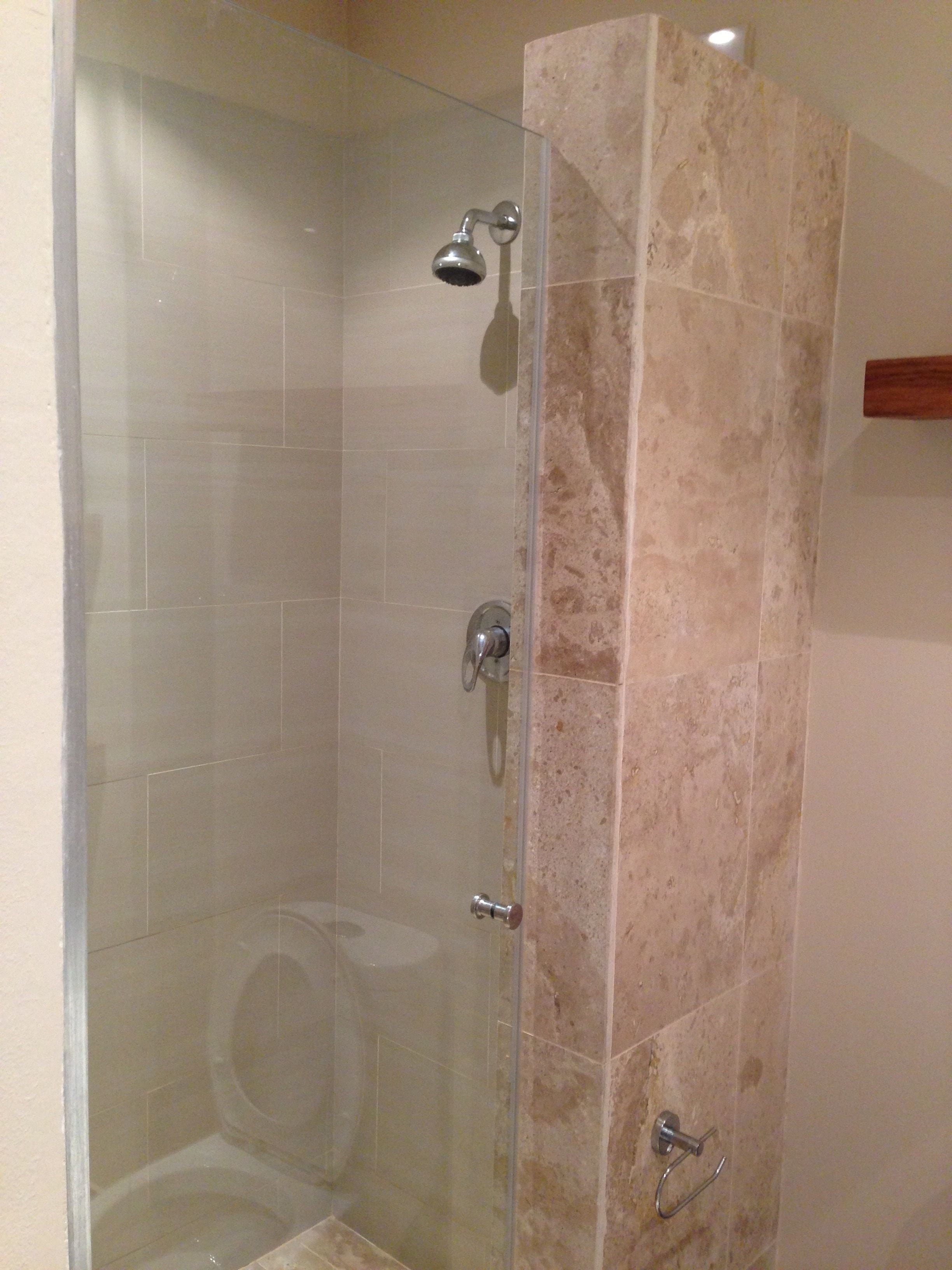 A glass-enclosed shower with a marble wall, a handheld showerhead, and a handheld faucet.