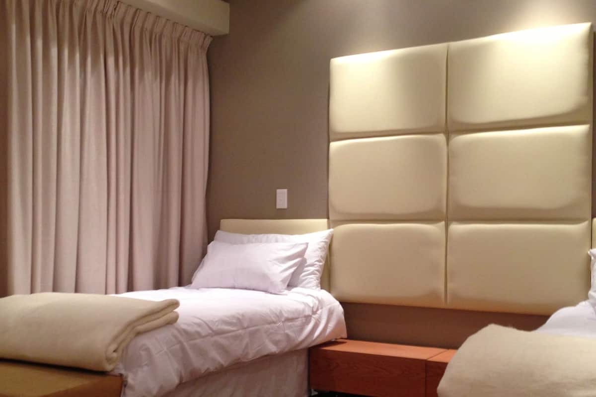 A modern hotel room with a large bed, a smaller sofa bed, wooden flooring, and a headboard with built-in lighting.