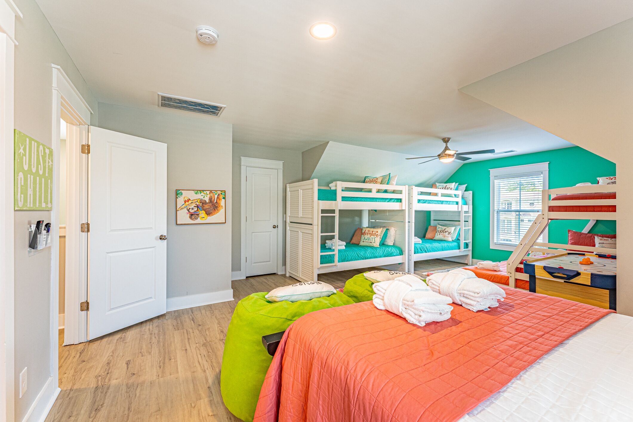 Une chambre avec des lits superposés, un ventilateur de plafond et un pouf vert.