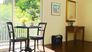 Una habitación con una mesa de comedor y sillas, una pequeña mesa con lámpara, un cuadro en la pared y una ventana con vistas a zonas verdes.