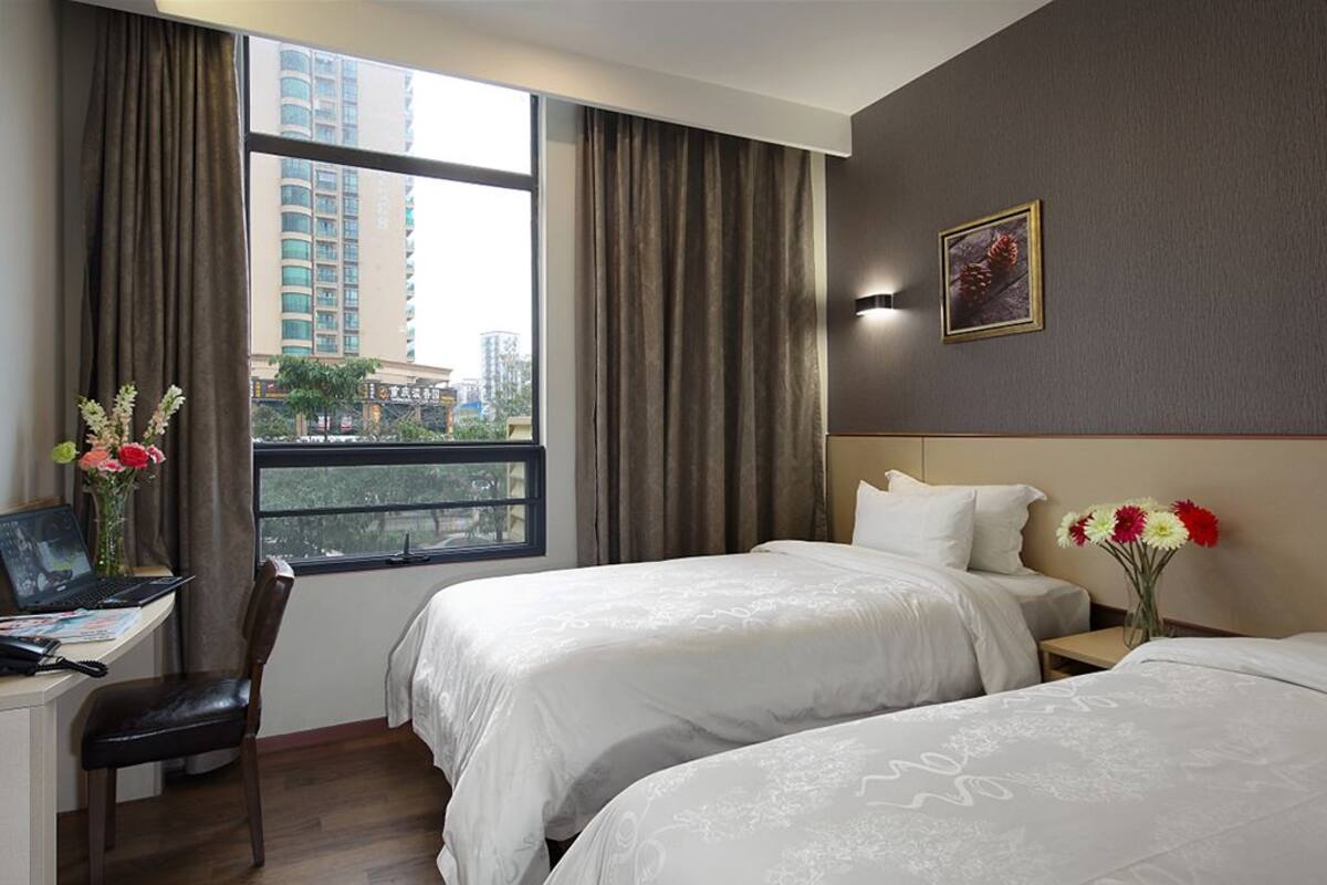 A hotel room with two beds, a desk with a laptop, a chair, and a window with curtains.