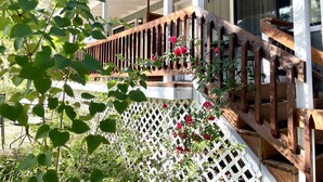A wooden deck with a white lattice fence, a wooden railing, and red flowers. - Garden Suite - Sierra Mountain Lodge (Ahwahnee)