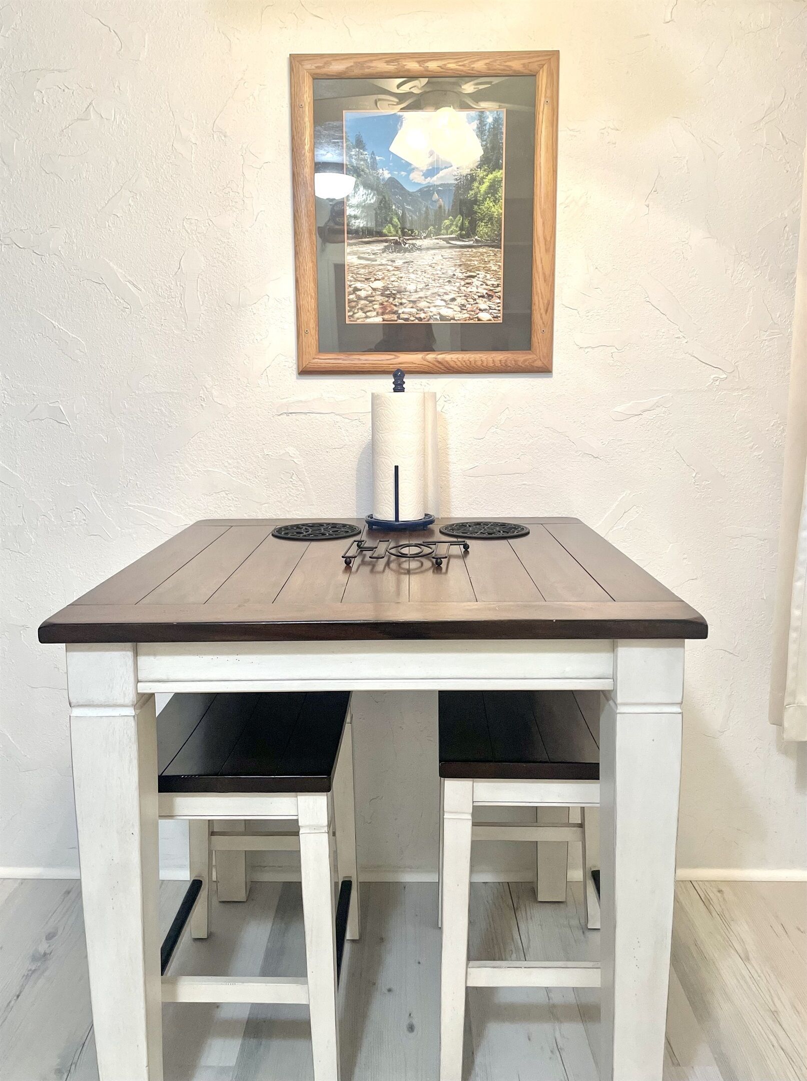 A dining table with a wooden top and white base, a framed picture above it, and a candle holder in the center.