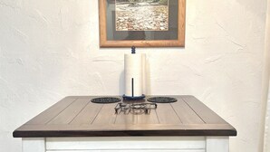 A dining table with a wooden top and white base, a framed picture above it, and a candle holder in the center.