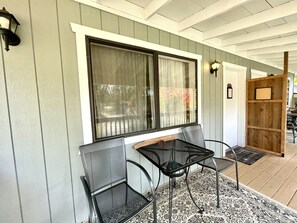 Une véranda couverte avec une table et des chaises, une fenêtre avec un rideau et une clôture en bois.